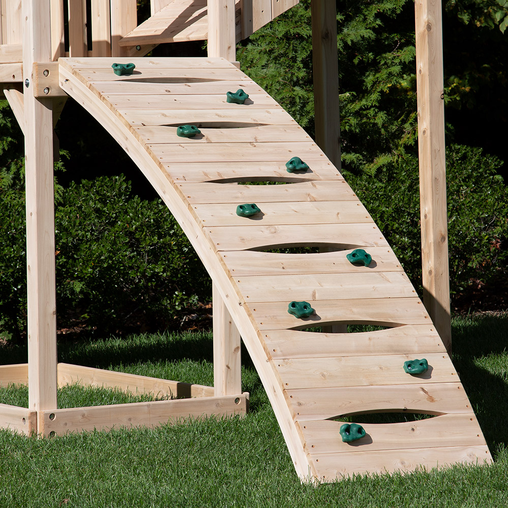 Arched wooden swing set rock wall with green rock holds.