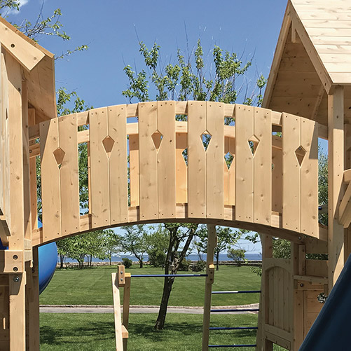 A arched bridge connecting two cedar swing set forts.