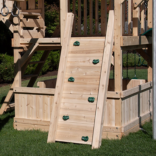 Narrow wooden swing set rock wall with green rock holds.