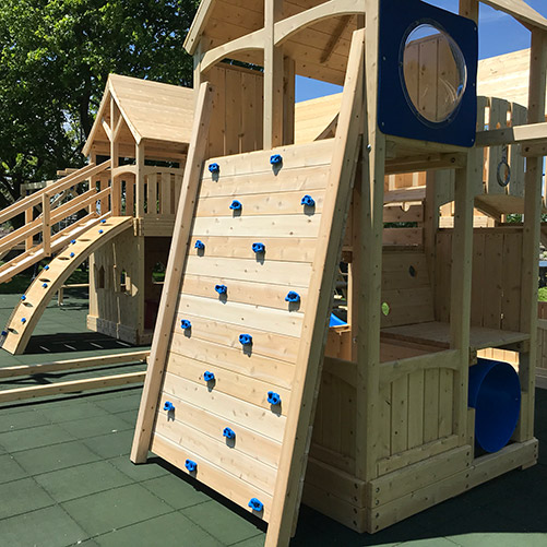 Wide wooden swing set rock wall with green rock holds.