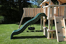 Green slide on wooden swing set.