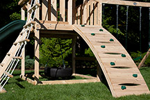 Triumph Play System's Kelton Climber cedar swing set with arched rock wall.