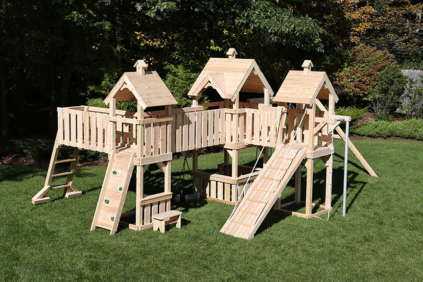 Backyard wooden swing set with three towers and bridges.