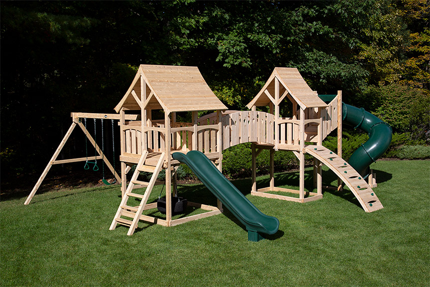 Cedar swing set with two forts connected with a arched bridge with a green tube slide.