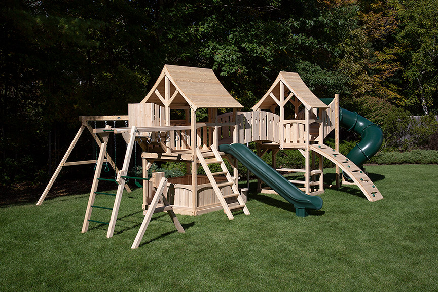 Cedar swing set with two forts connected with a arched bridge with a green tube slide.