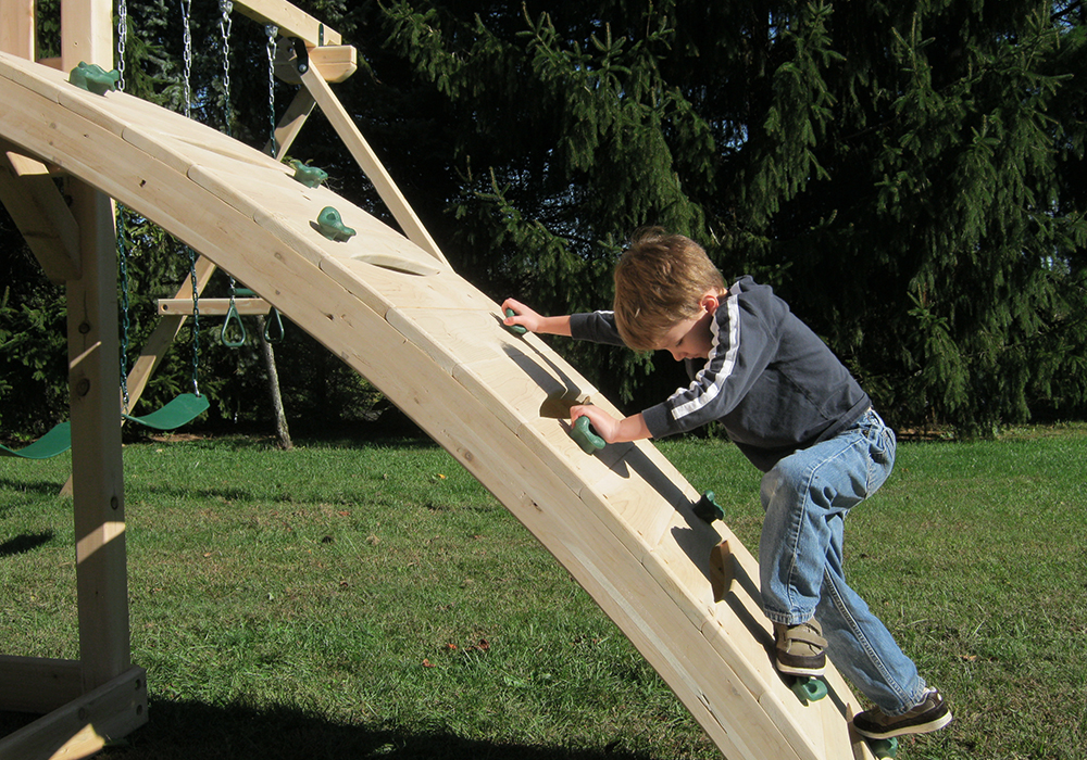 Triumph Play System's Kelton Climber cedar swing set with arched rock wall and rope ladder.